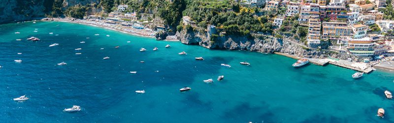 Aerial drone view of the Tyrrhenian sea coast in Positano, Italy. Multiple classic buildings on rocky cliffs, a lot of greenery