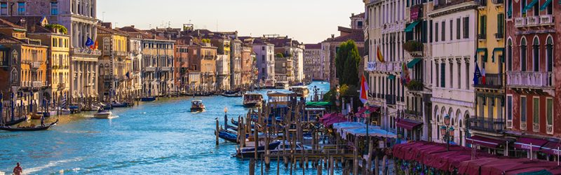 View of facades of picturesque old buildings on the Grand Canal, gondolas and boats in Venice. Sunny summer day with blue sky.